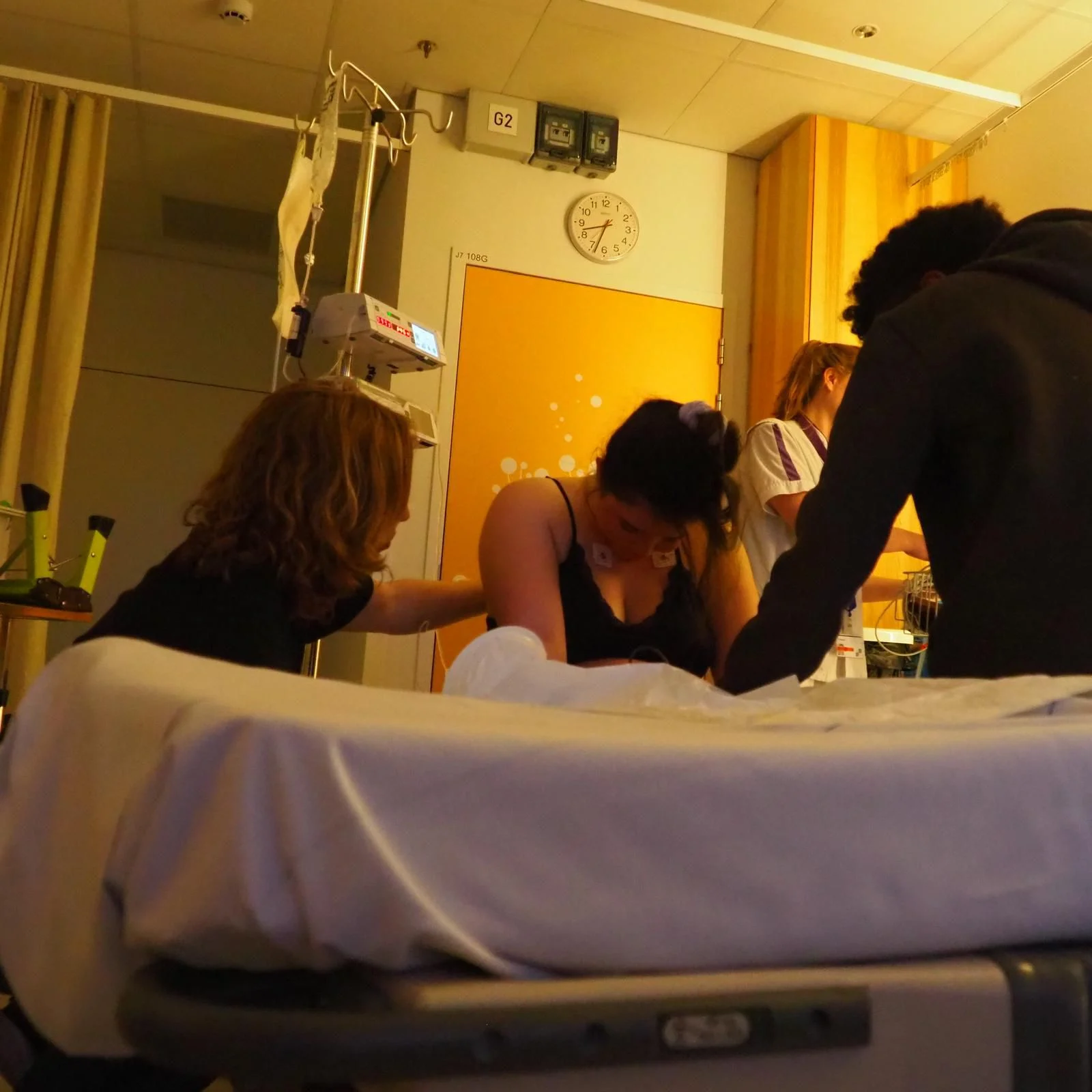 Birthing position: leaning forward Woman in labour leaning forward on the hospital bed, with doula Iris and her partner beside her