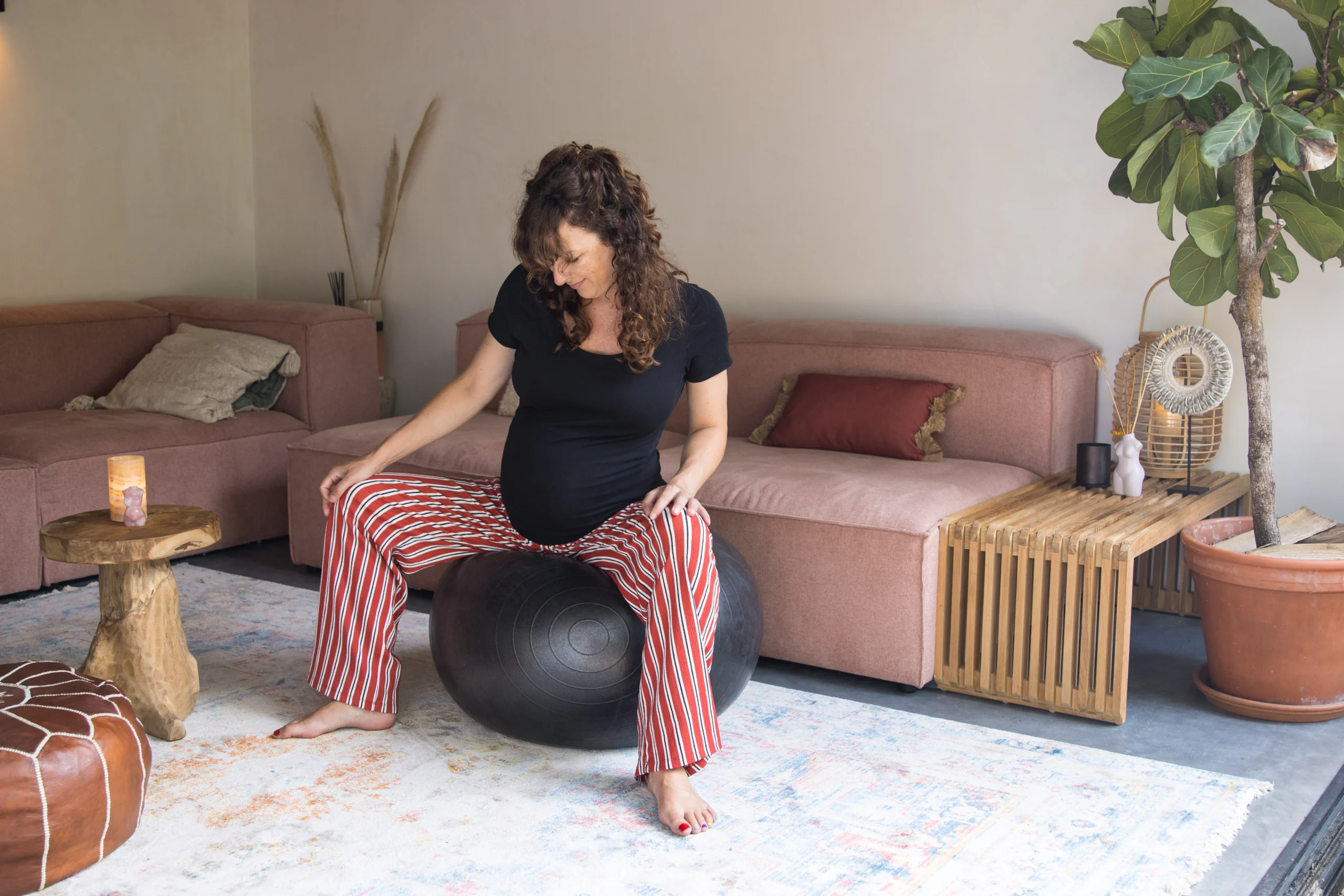 Pregnant woman practising on a birth ball in the living room to prepare for labour